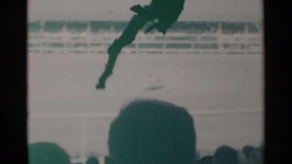A horse and rider move across the dirt track while a large foreground spectator silhouette partially blocks the lower frame.