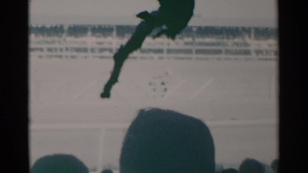 Jockey on a galloping horse passes a racetrack as spectator heads fill the foreground.