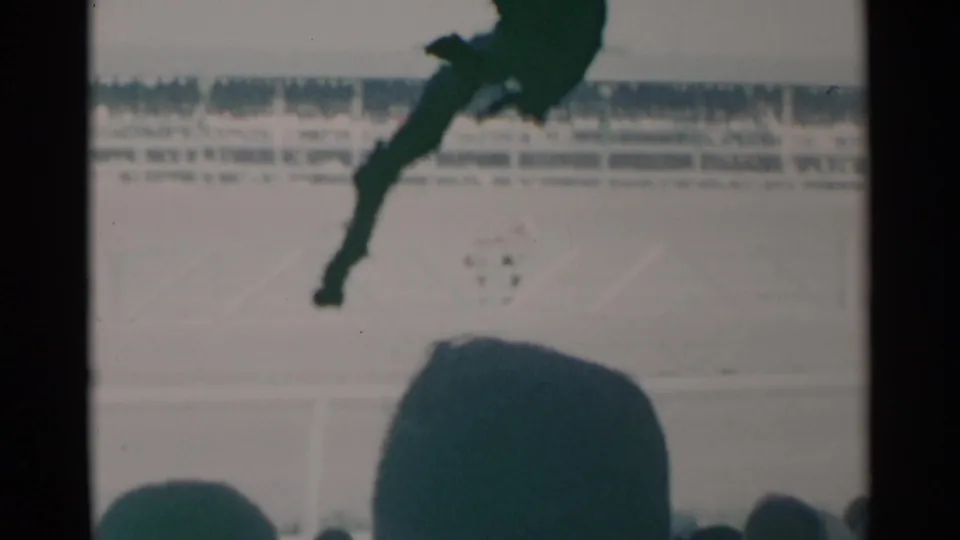 1960 Cheyenne home-movie frame showing a jockey and horse on a bright racetrack, viewed over silhouetted spectators.