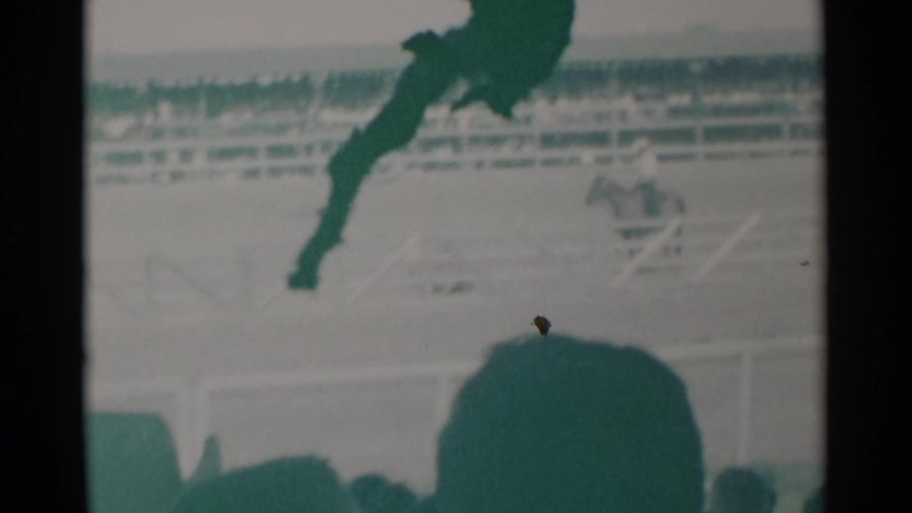Mounted rider crosses the arena behind silhouetted spectators.