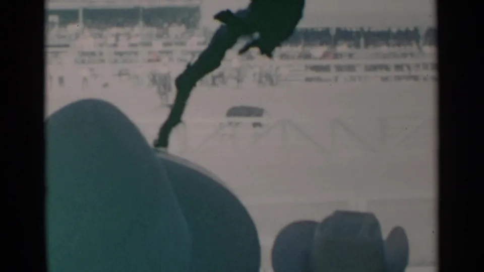 1960 Cheyenne home-movie frame of horse-and-rider action in an outdoor arena, with spectator heads and bleachers visible.