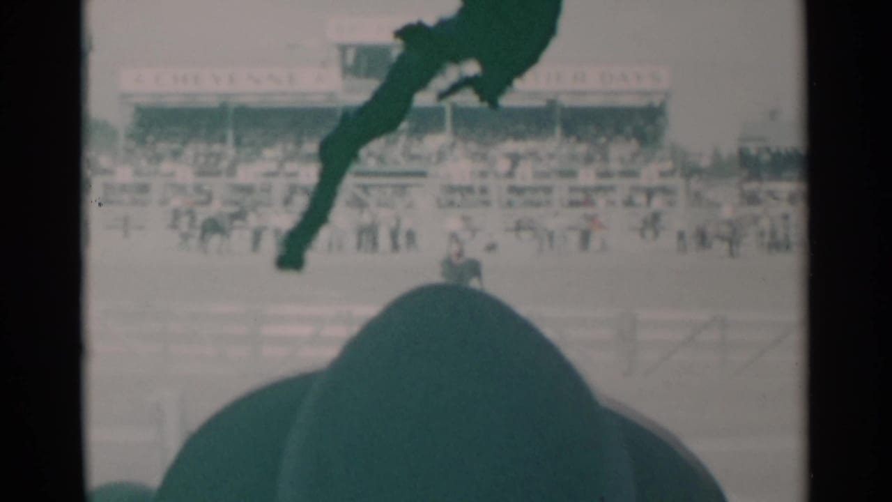 1960 Cheyenne, Wyoming rodeo footage shows a soft, green-tinted arena view with spectators, a rider on horseback, fencing, and dark foreground obstruction from the filming position.