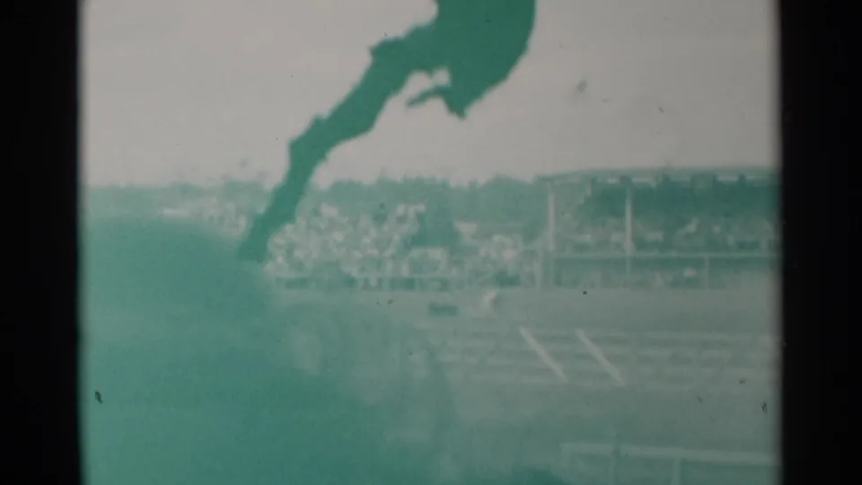 Green-tinted 8mm frame of the Cheyenne rodeo arena, with a dark steer and spectators beyond the fence.
