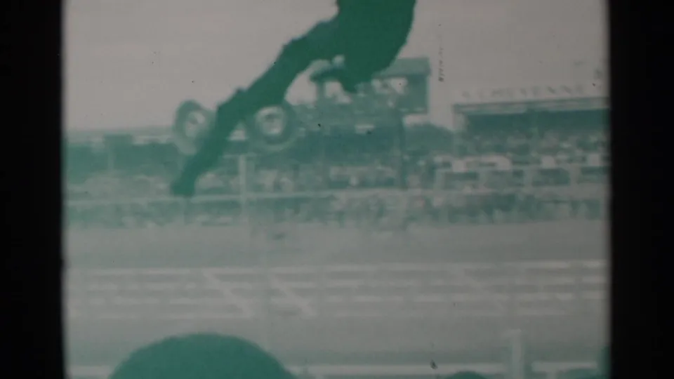 1960 Cheyenne home-movie frame with horses racing in front of packed bleachers, partially blocked by foreground spectator silhouettes.