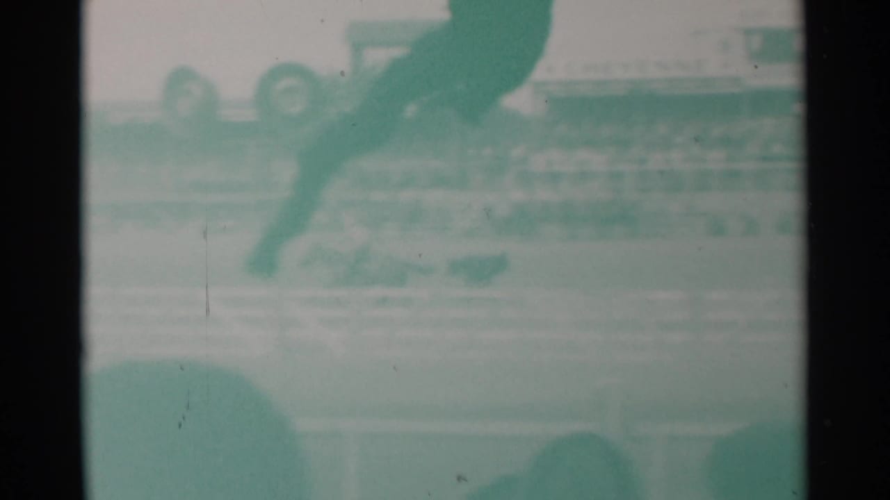 Faded 8mm frame from the Cheyenne rodeo clip with a horse and rider entering the upper frame above arena rails and stands.