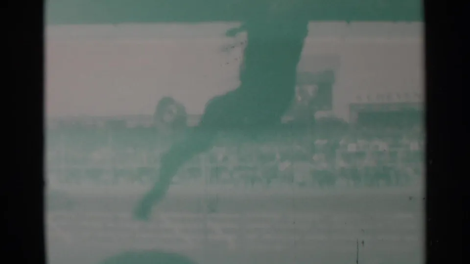 A blurred horse and rider move across the Cheyenne rodeo arena, with spectators and railings visible through faded 8mm color.