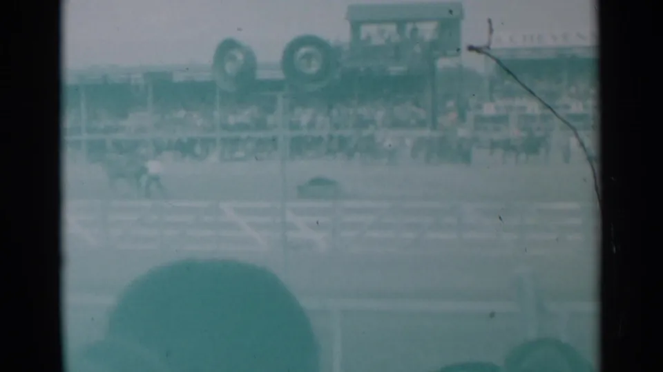 1961 Cheyenne rodeo frame with a rider in the arena, packed grandstand seating, rail fencing, and indistinct signage or vehicles above the crowd.