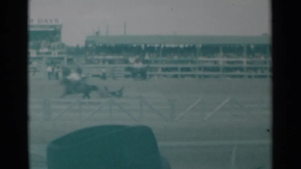 1961 Cheyenne rodeo frame showing riders moving across the arena with white rail fencing and a broad spectator stand behind them.