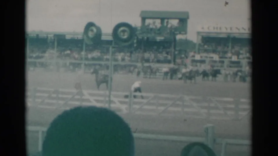 1961 Cheyenne rodeo arena view with mounted riders before a crowded grandstand, partly blocked by a foreground spectator.