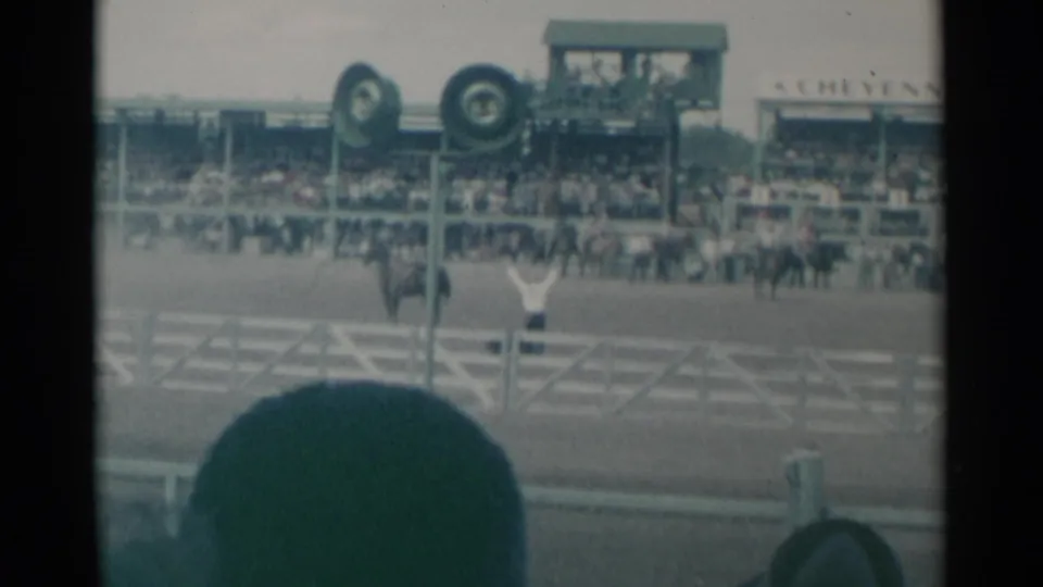 Cheyenne Frontier Days arena moment with a mounted rider or official raising arms before the grandstand crowd.