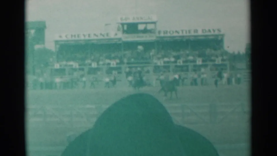 Cheyenne Frontier Days arena view in green-tinted 8mm, with riders and horses partly obscured by a foreground spectator.
