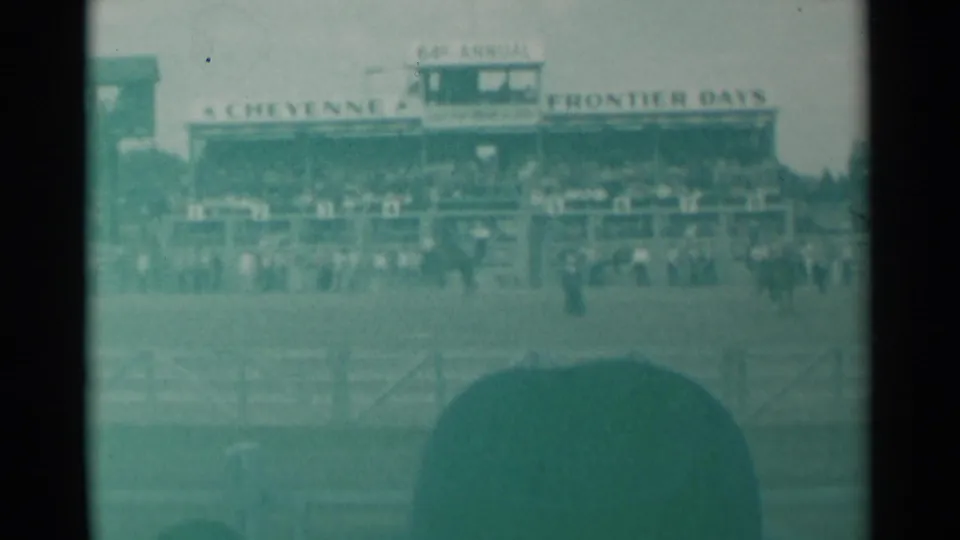 Cheyenne Frontier Days grandstands and arena spectators are seen through hazy 8mm color, with a large hat partly blocking the lower frame.