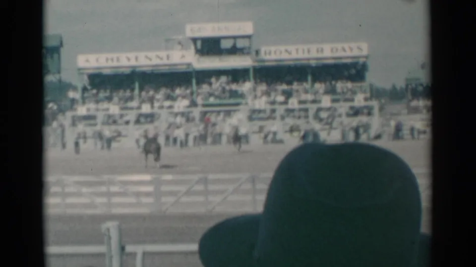 Cheyenne Frontier Days arena view with one rider near the fence, crowded grandstands, event signage, and a dark foreground silhouette.