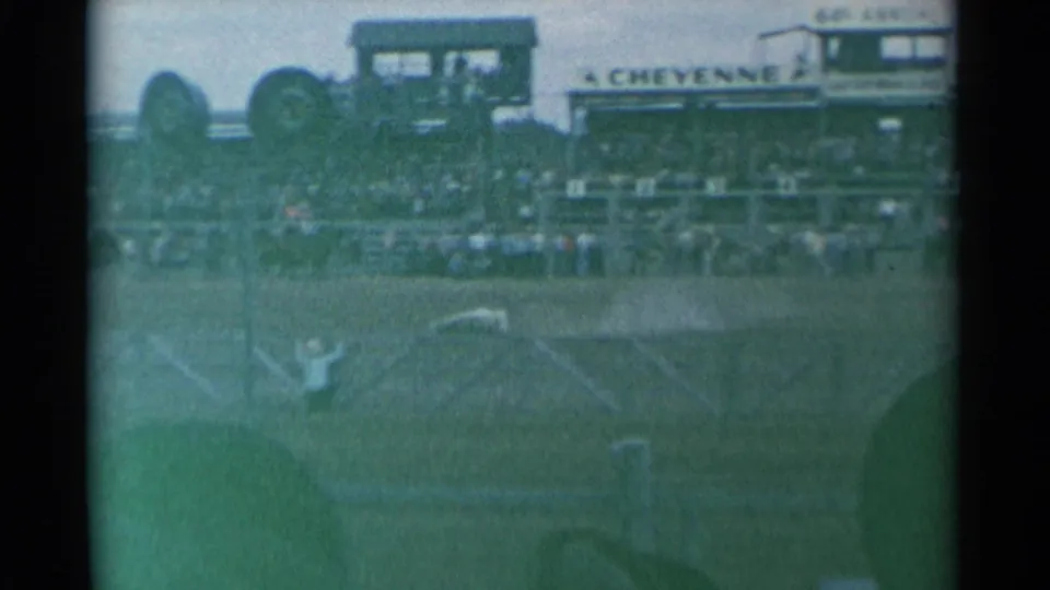 Faded 8mm view of the Cheyenne Frontier Days grandstand area, with signage above the crowd and arena fencing in the foreground.