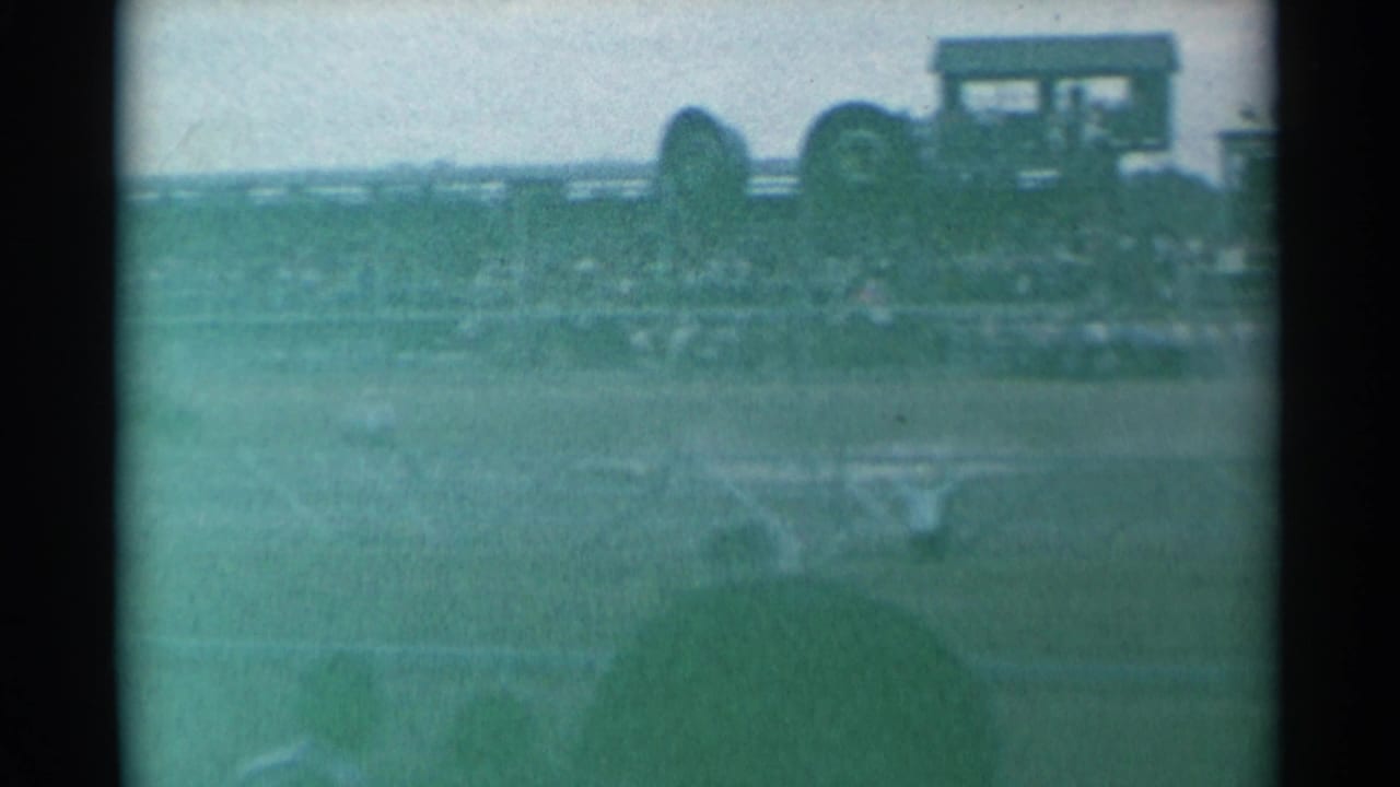 Soft 8mm view of a rodeo arena with spectators and a raised booth in the distance.