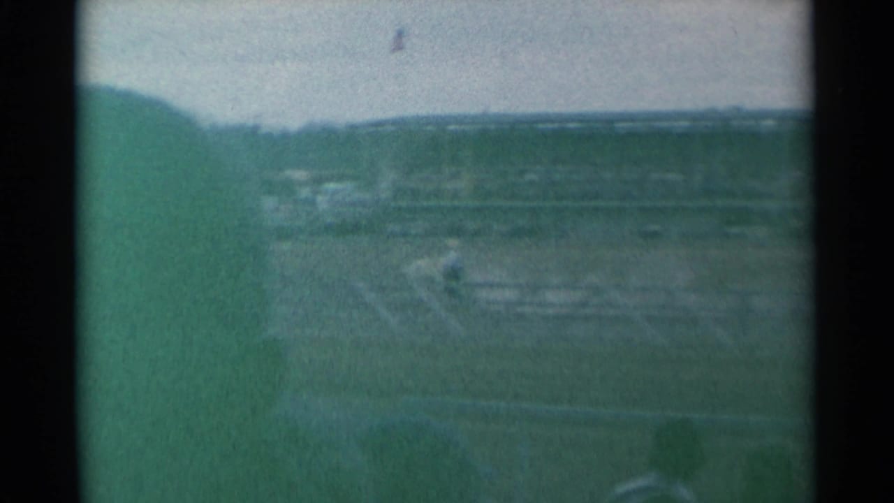Soft 8mm frame of the Cheyenne rodeo grounds, showing arena space, fence lines, and distant spectator areas under a bright sky.