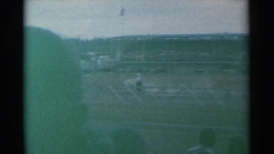 Soft 8mm frame of the Cheyenne rodeo grounds, showing arena space, fence lines, and distant spectator areas under a bright sky.
