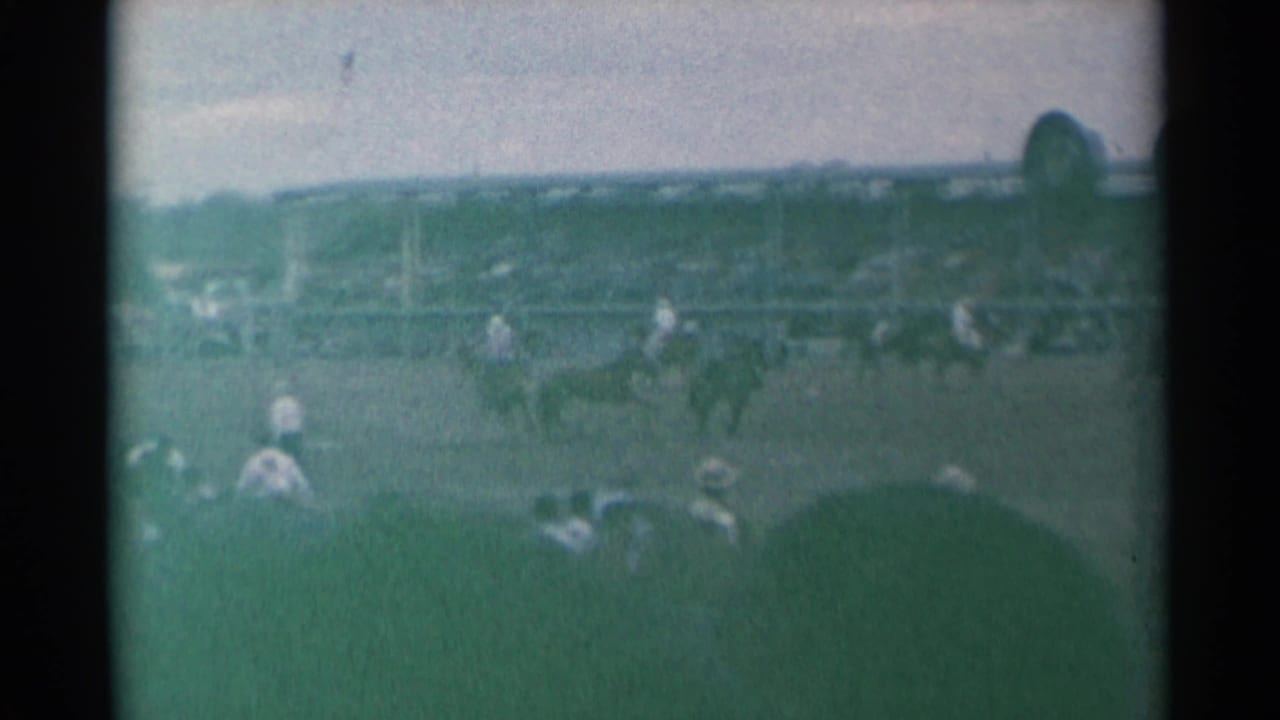 Wide 1961 Cheyenne rodeo view with horseback riders moving across the arena as spectators watch from the stands.