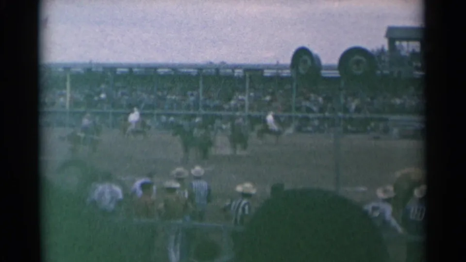 Cheyenne rodeo footage from 1961 showing a rider on horseback near the fence, filmed over spectators' hats from the stands.