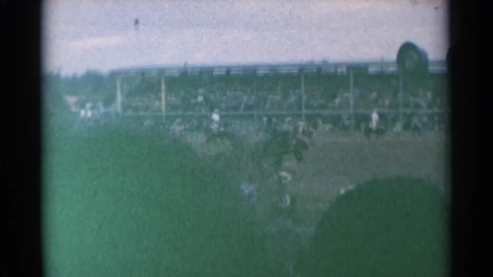 Wide 1961 Cheyenne rodeo frame with riders in the arena, crowded stands behind them, and spectator heads in the foreground.