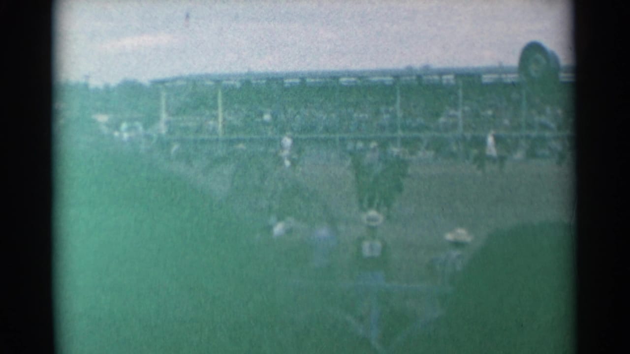 Rodeo arena with riders, spectators in grandstands, and green-tinted film haze.