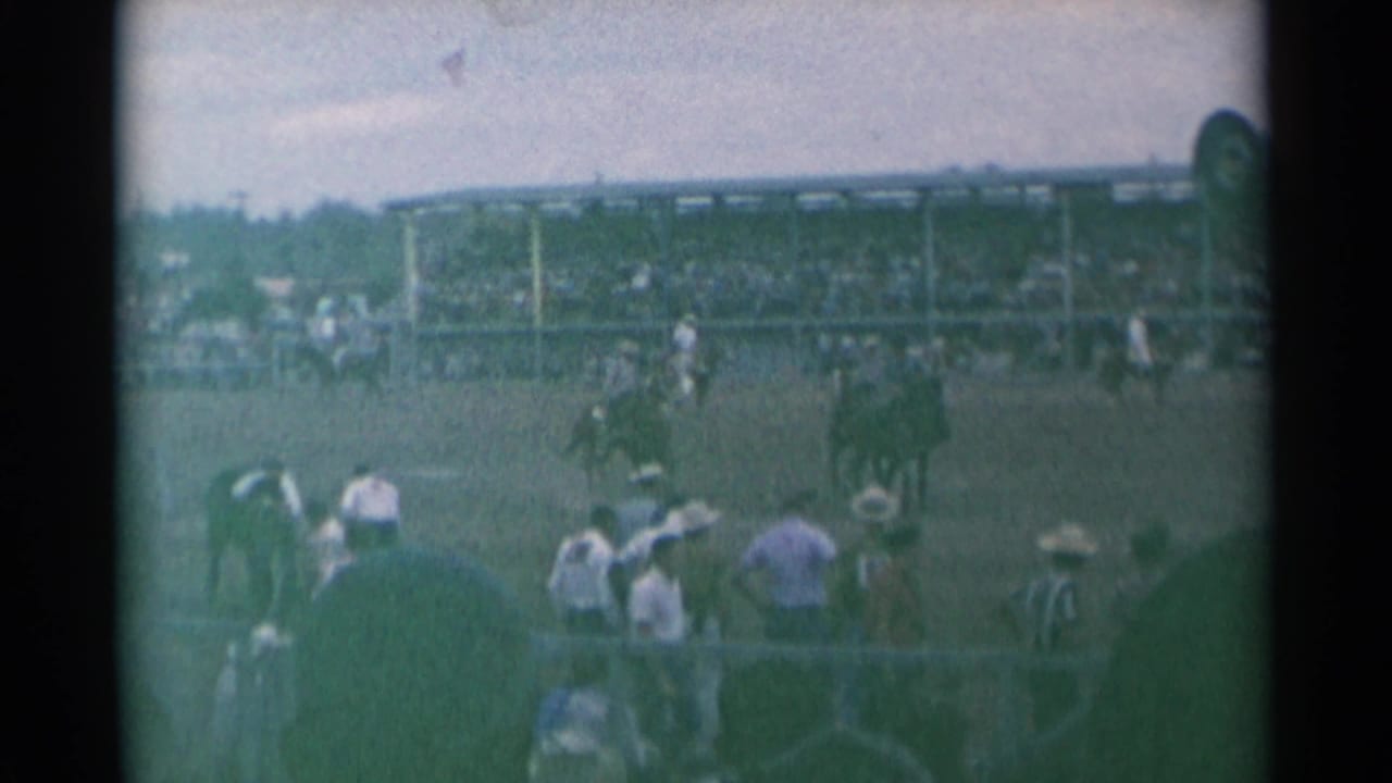 Cowboys and horses in a rodeo arena with filled grandstands behind them.