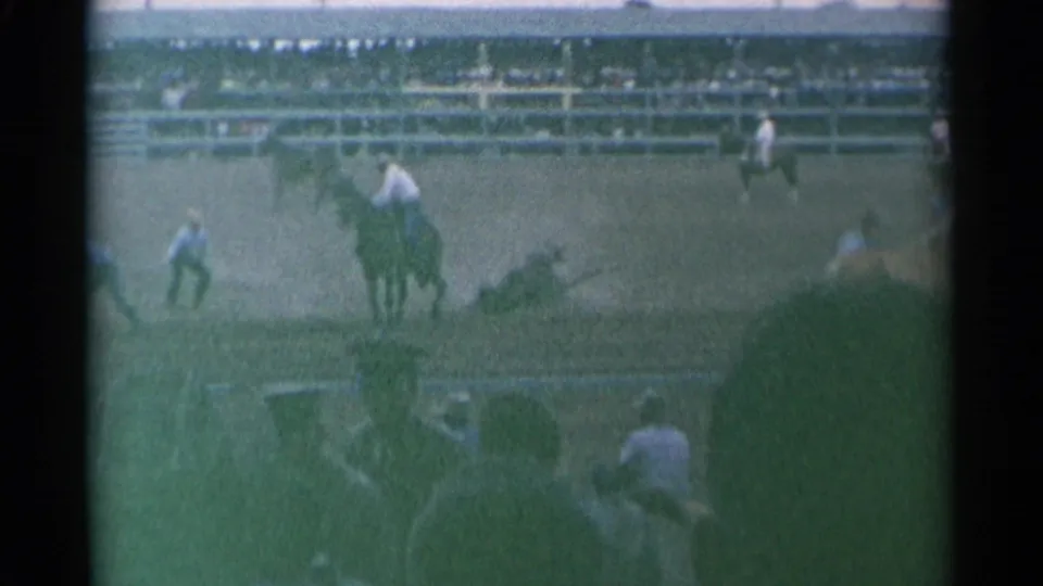 A mounted rider crosses the Cheyenne rodeo arena while spectators watch from the long grandstand beyond the fence.