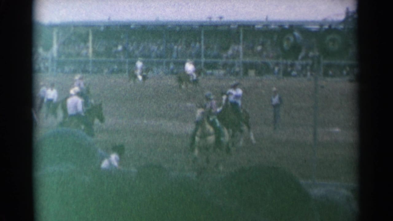 Bucking horse action in a rodeo arena with cowboys and spectators nearby.