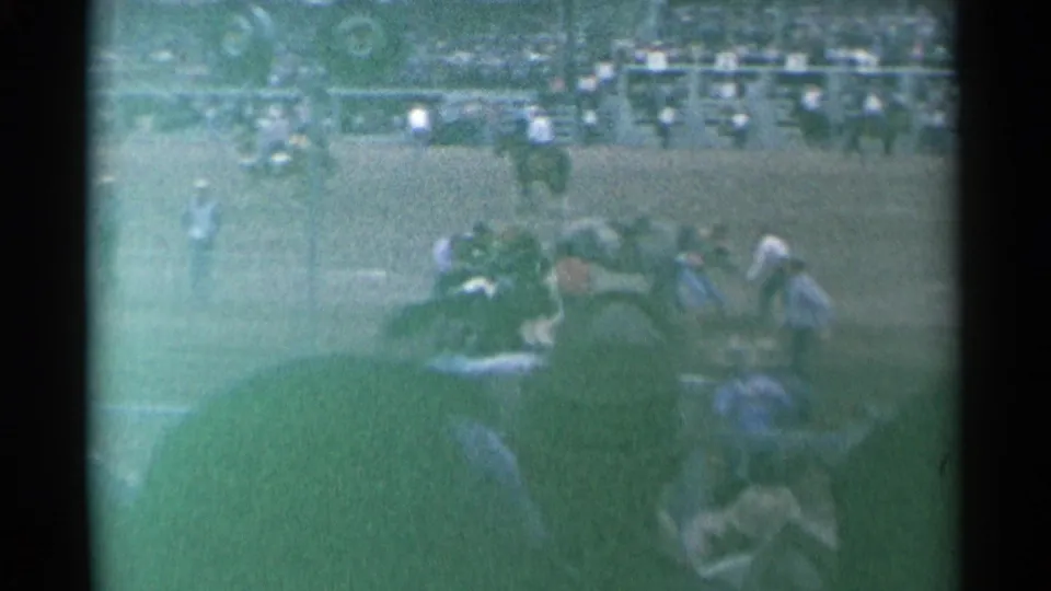 A horse and several rodeo participants are seen near the rail at the 1961 Cheyenne arena, with crowded stands behind them.