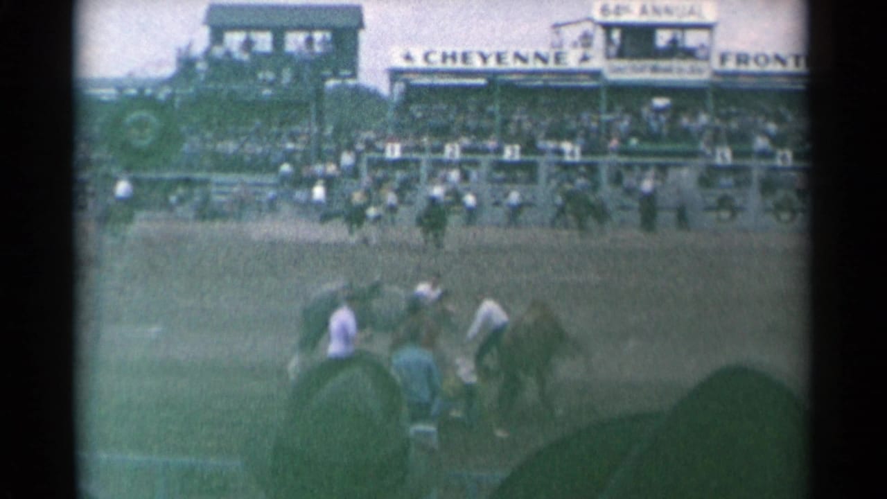 Cowboys and horses in a rodeo arena with grandstands behind them.