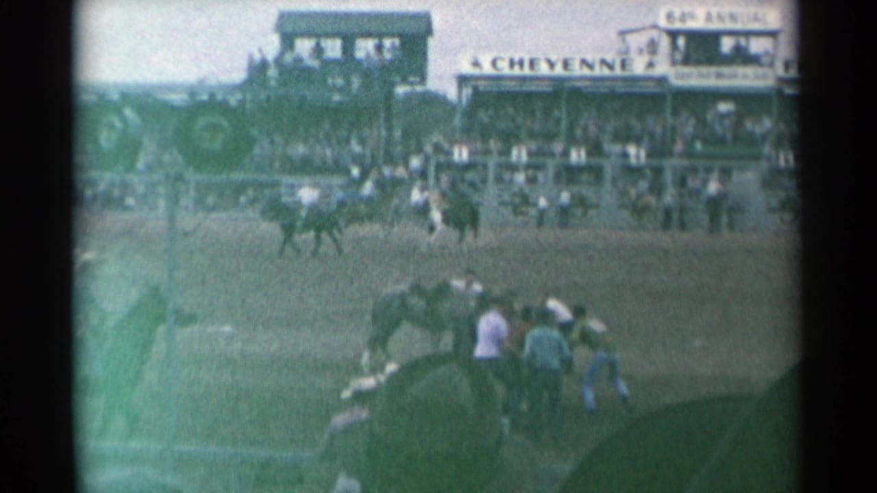 Home-movie view of the Cheyenne rodeo arena with mounted riders, nearby horses and spectators in the stands.