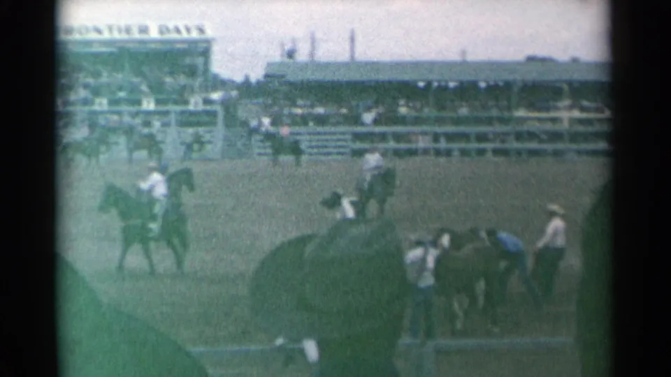 Cheyenne rodeo home-movie frame showing horseback activity in the arena with crowded grandstands in the background.