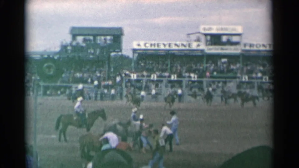 Wide 1961 Cheyenne Frontier Days view with riders and horses in the arena below grandstands carrying visible Cheyenne and Frontier Days signage.