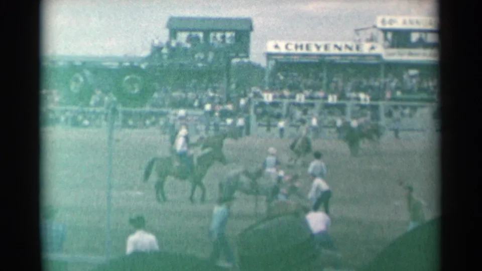Cheyenne Frontier Days arena view with mounted riders, horses, spectators, and large grandstand signage visible through green-tinted 8mm film.