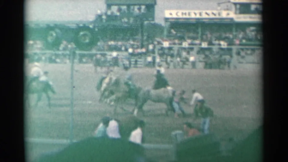 A Cheyenne rodeo arena view shows a horse and rider moving across the dirt, with spectators and signage visible beyond the fence.