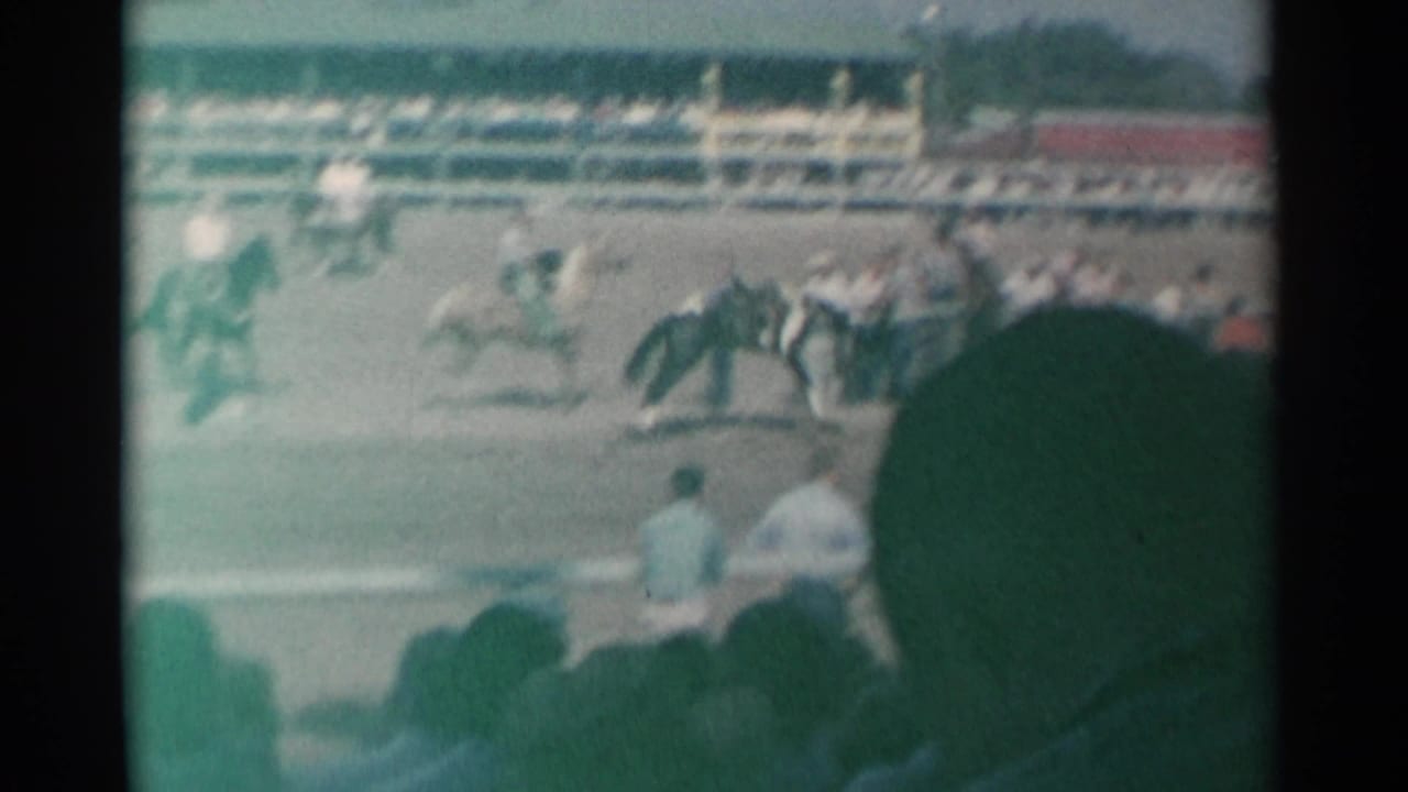 1961 Cheyenne rodeo view with riders in a dusty arena, fencing, grandstand seating, and spectators partly silhouetted in the foreground.