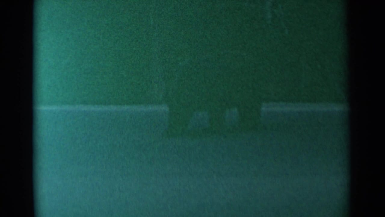 1961 Cheyenne 8mm frame with heavy grain, green cast, and a dim outdoor field where the subject is not clearly defined.