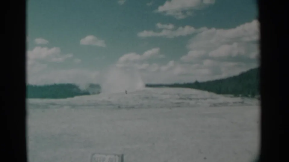 Distant geyser plume appears against a partly cloudy sky in this 1961 8mm travel view of a broad geothermal basin.