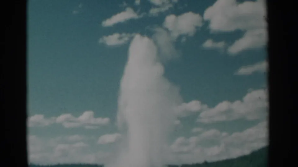 1961 8mm home-movie frame with a closer, soft-focus view of the geyser plume filling much of the frame beneath clouds.
