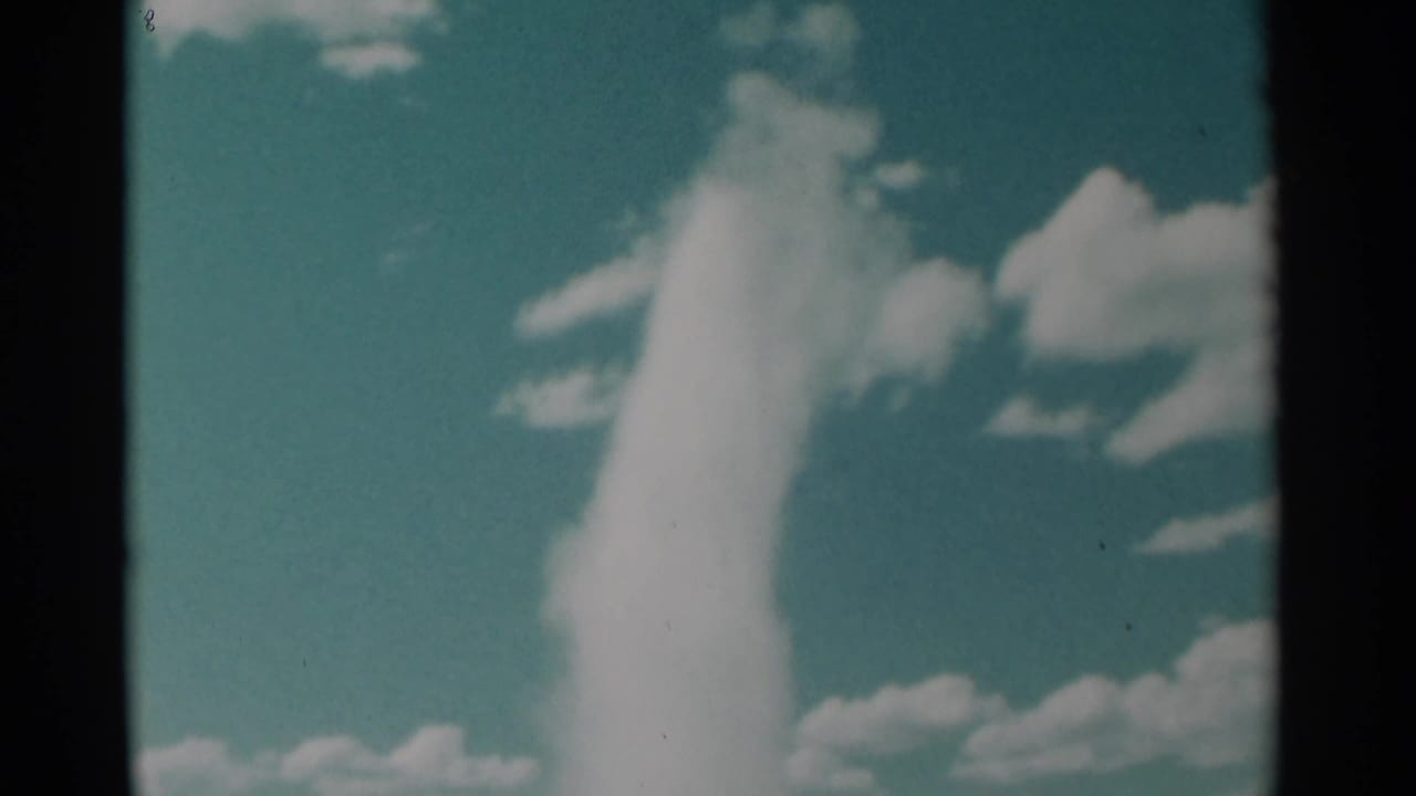 Geyser column climbing into a cloud-filled blue-green sky.
