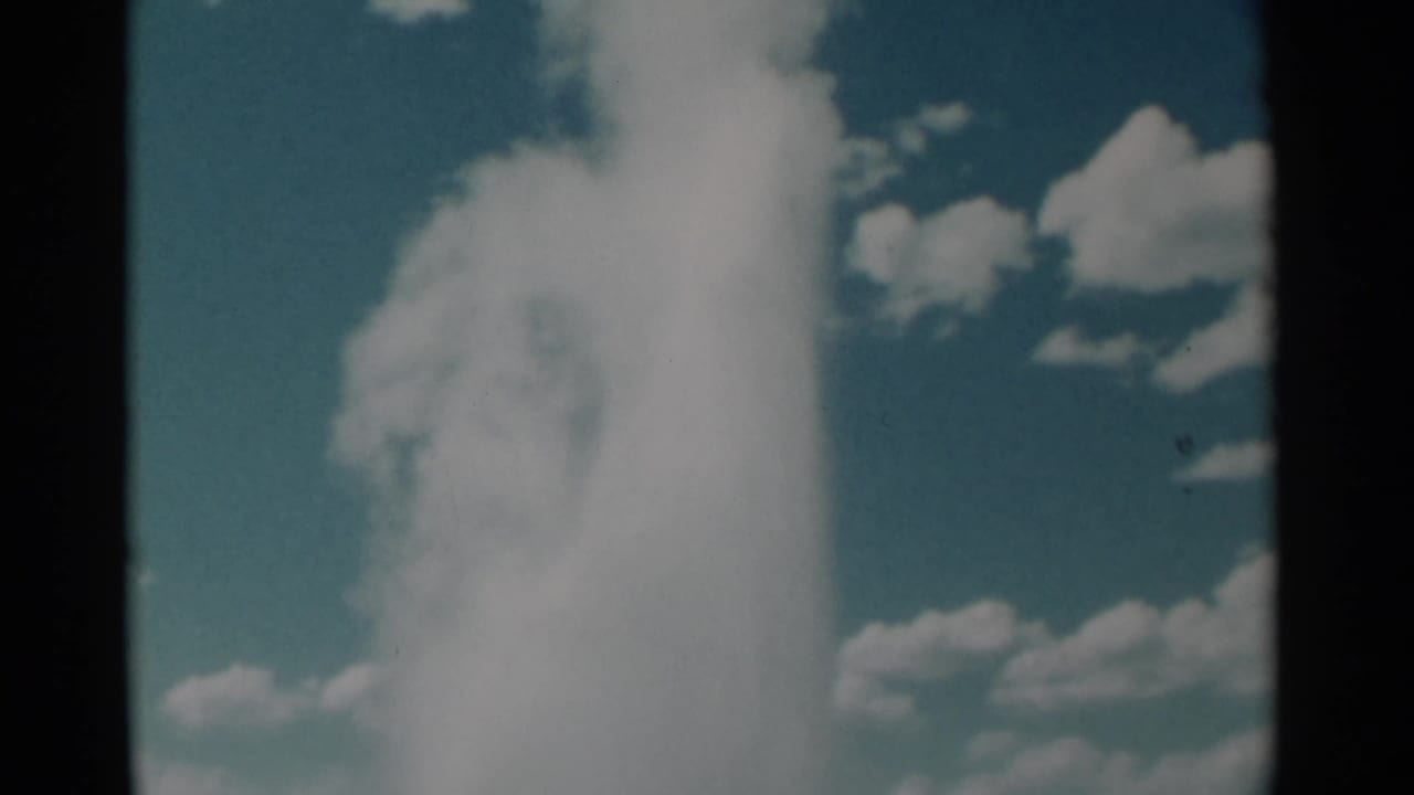 1961 8mm home-movie frame of a geyser-like steam plume rising into a blue sky, based on supplied Wyoming metadata.
