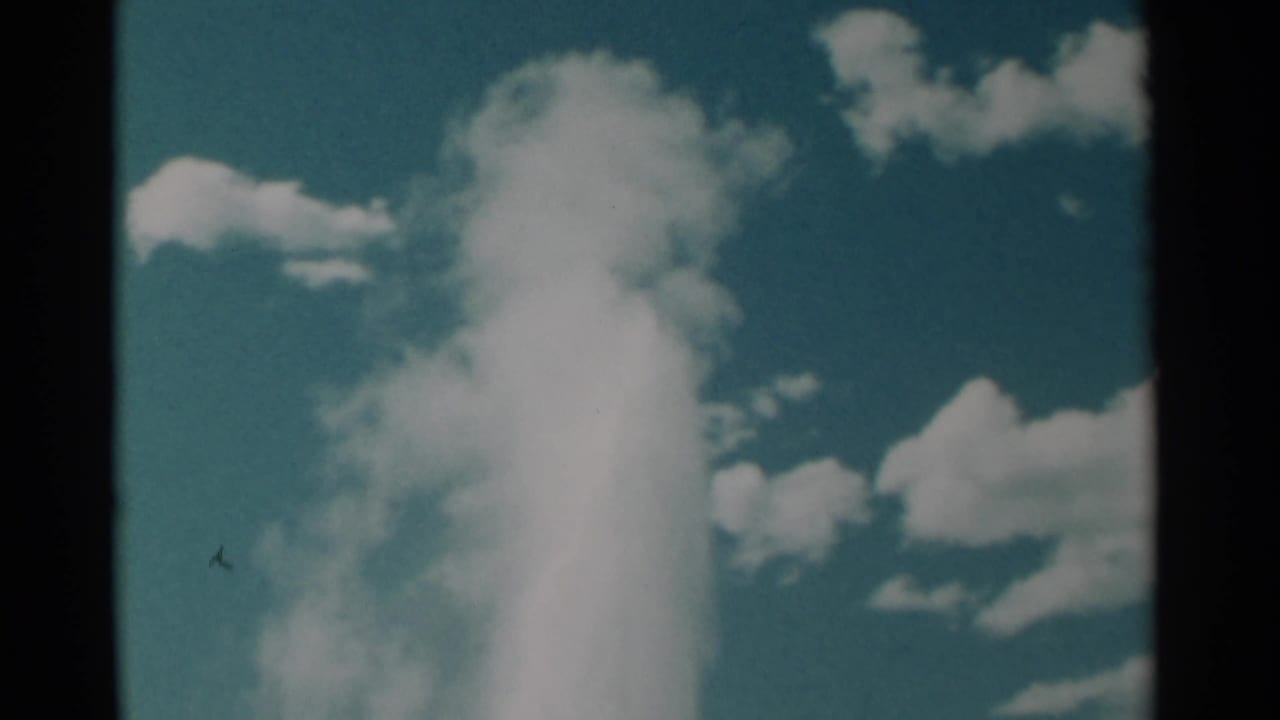 White steam column framed by blue sky, clouds, and dark film edges.