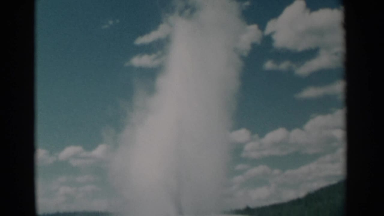 Tall white geyser plume rising against blue sky and clouds, with dark film-frame edges.