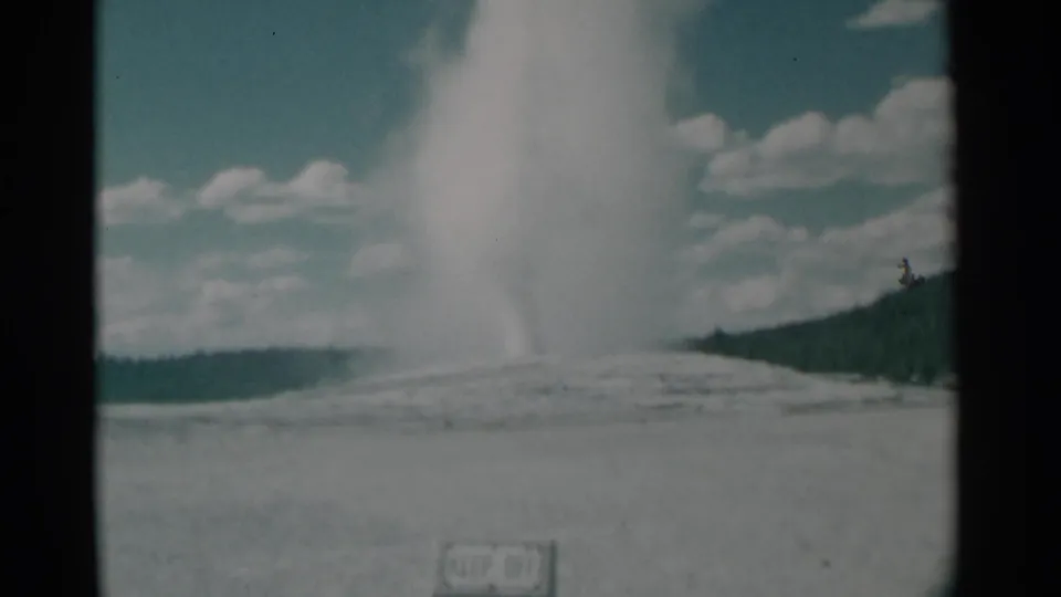 The geyser plume towers over open terrain in this 1961 Wyoming 8mm frame, with hills and clouds in the distance.