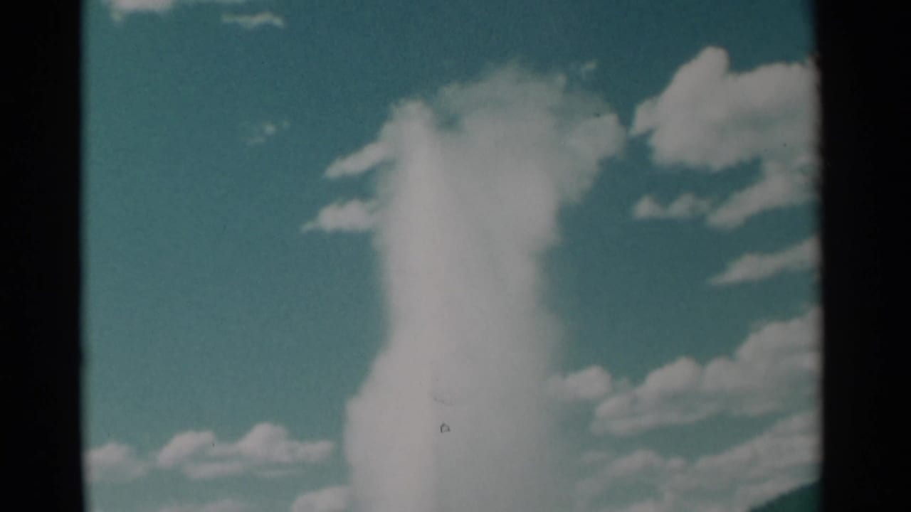 Tall geyser plume rising into a blue sky with scattered white clouds.