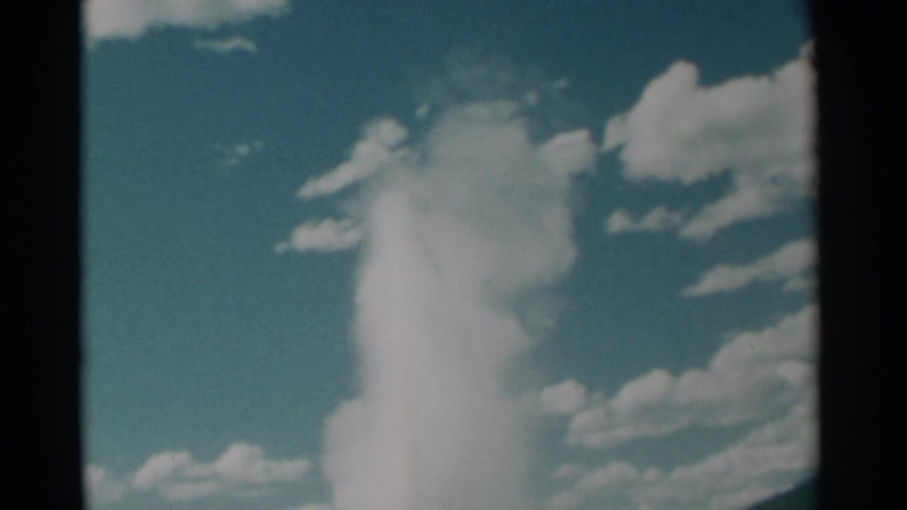 Geyser plume and steam cloud framed against a bright blue sky.