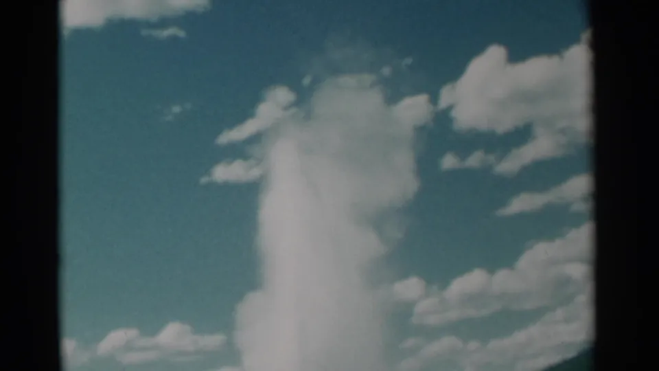 1961 Wyoming 8mm frame with a geyser plume spreading into mist beneath scattered white clouds.