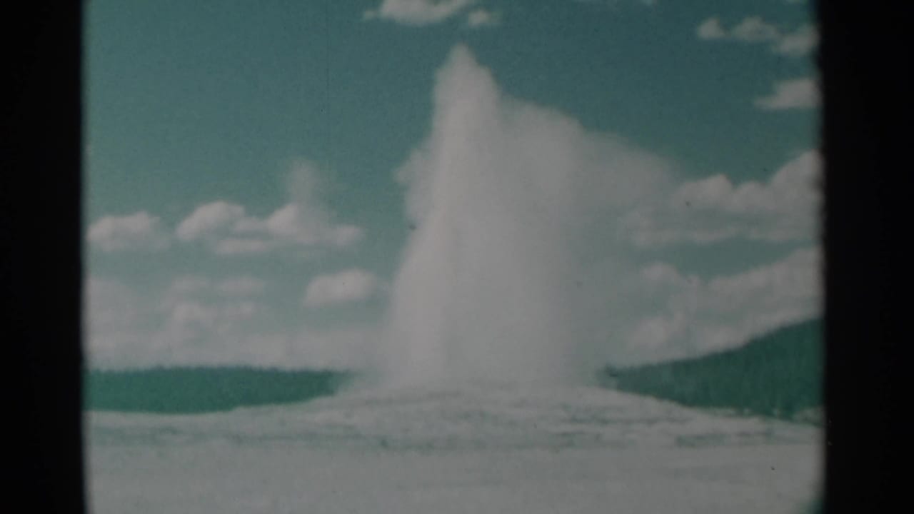 Old Faithful geyser erupting beneath a blue sky with scattered clouds.
