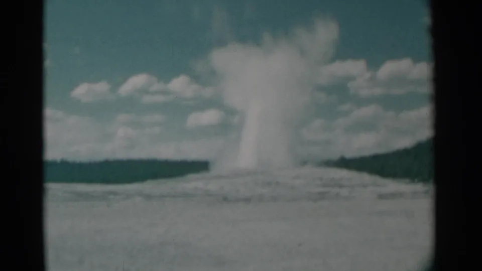 8mm frame from 1961 showing Old Faithful continuing to erupt, with a softer steam column and the Yellowstone landscape behind it.