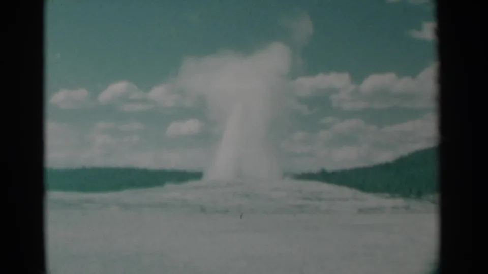 1961 8mm Yellowstone frame showing Old Faithful's plume spreading outward as steam drifts above the geyser basin.